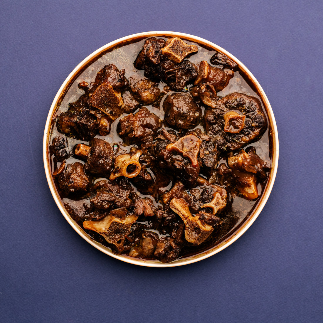 Birdseye view of Jamaican oxtail stew on a plate with a purple background